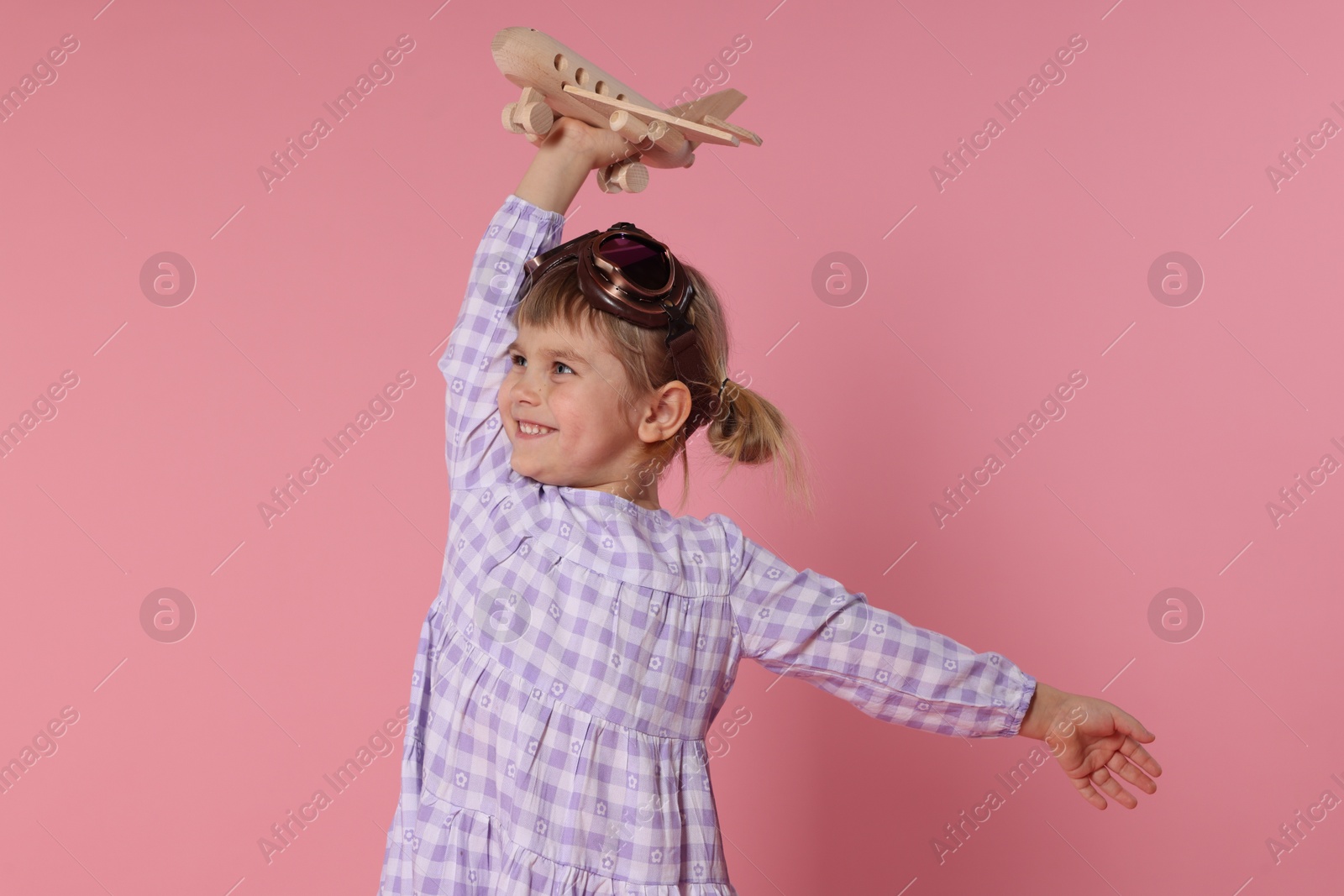 Photo of Happy little girl playing with toy plane on pink background