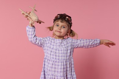 Photo of Cute little girl playing with toy plane on pink background