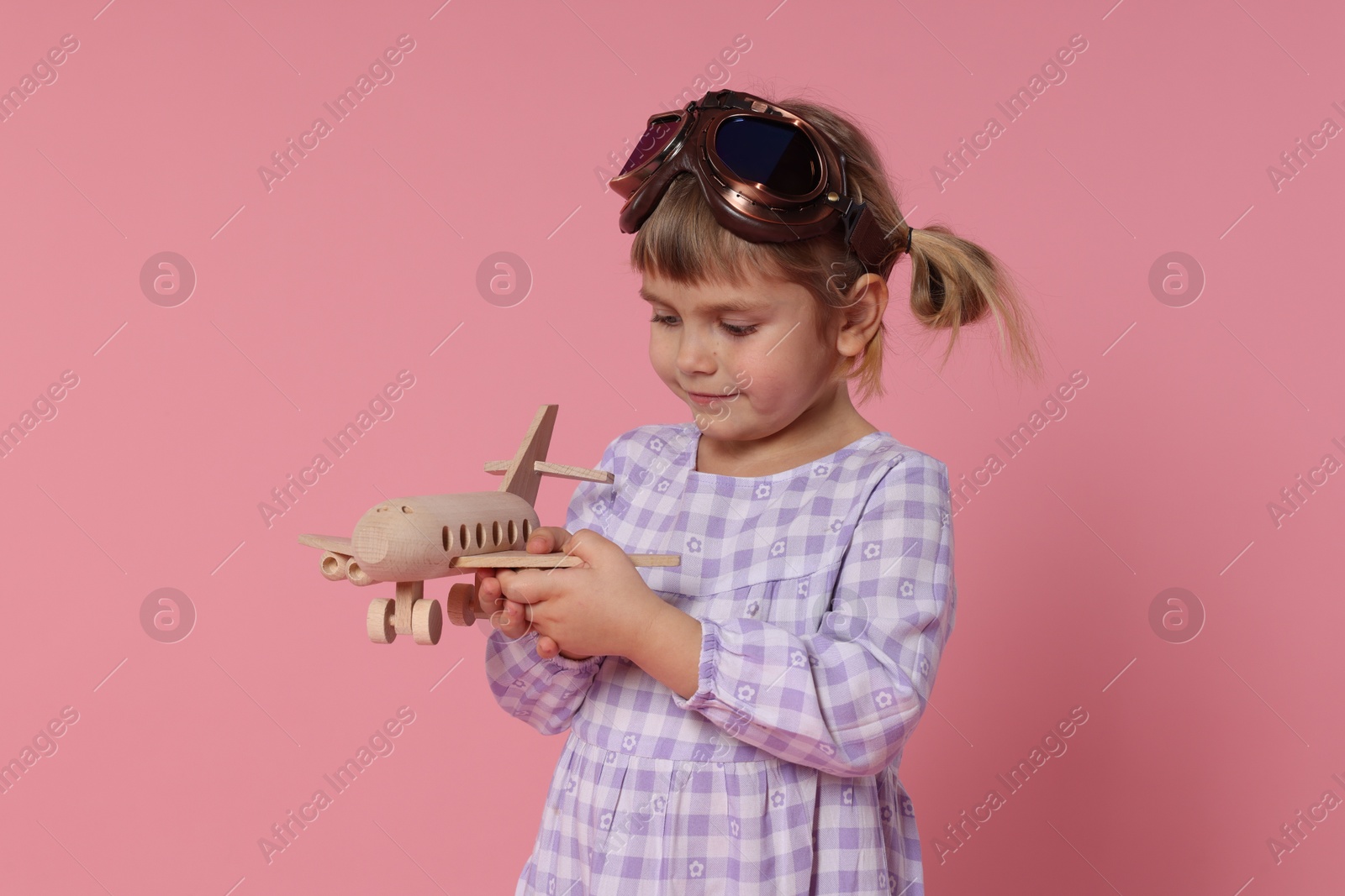 Photo of Cute little girl playing with toy plane on pink background