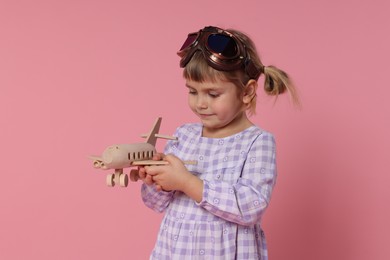 Cute little girl playing with toy plane on pink background