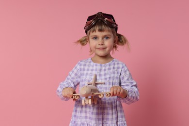 Photo of Cute little girl playing with toy plane on pink background