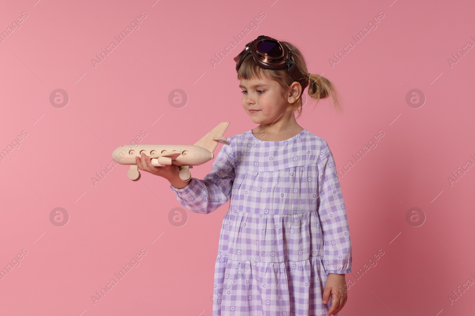 Photo of Cute little girl playing with toy plane on pink background