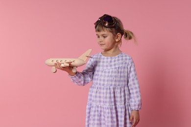 Cute little girl playing with toy plane on pink background