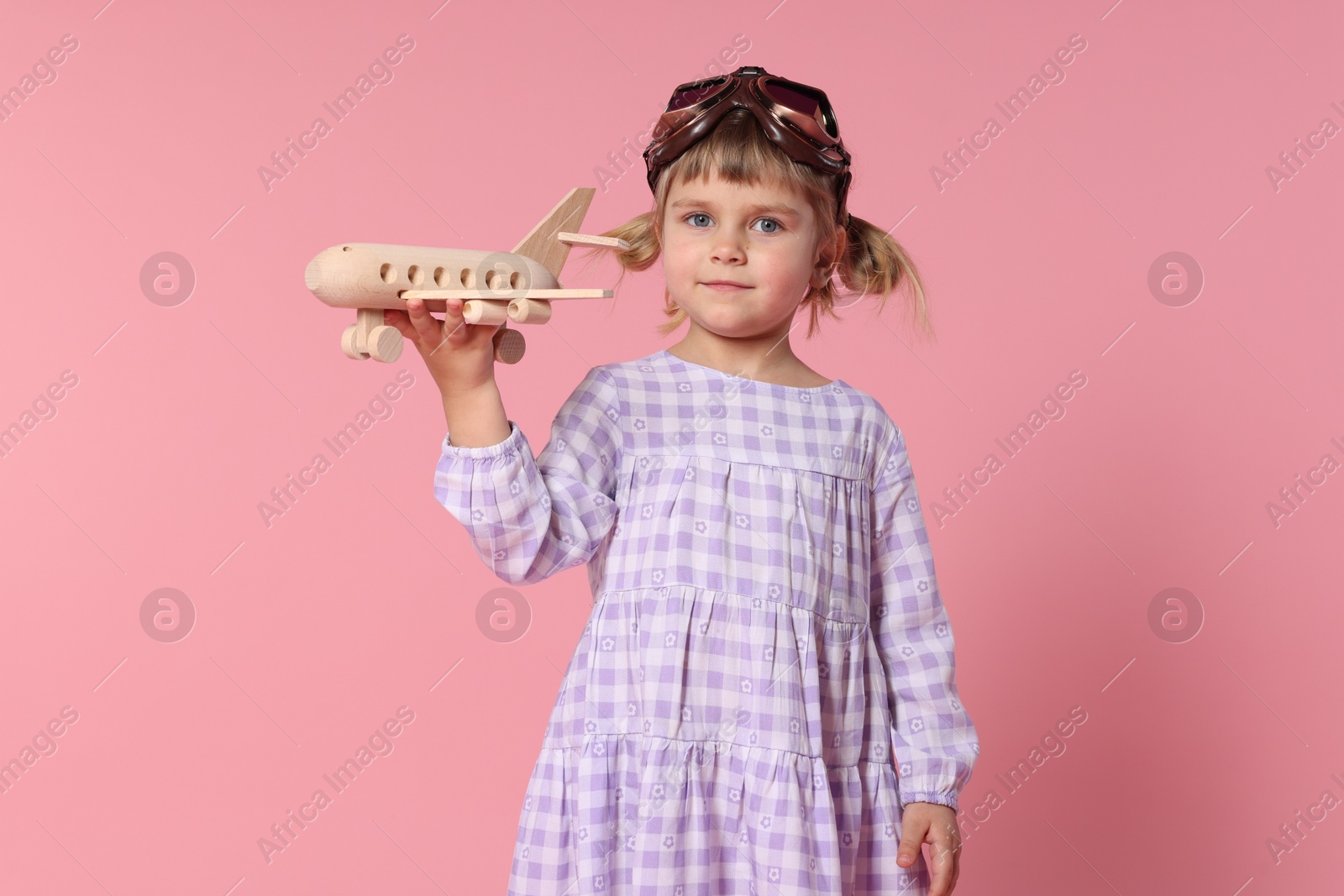 Photo of Cute little girl playing with toy plane on pink background