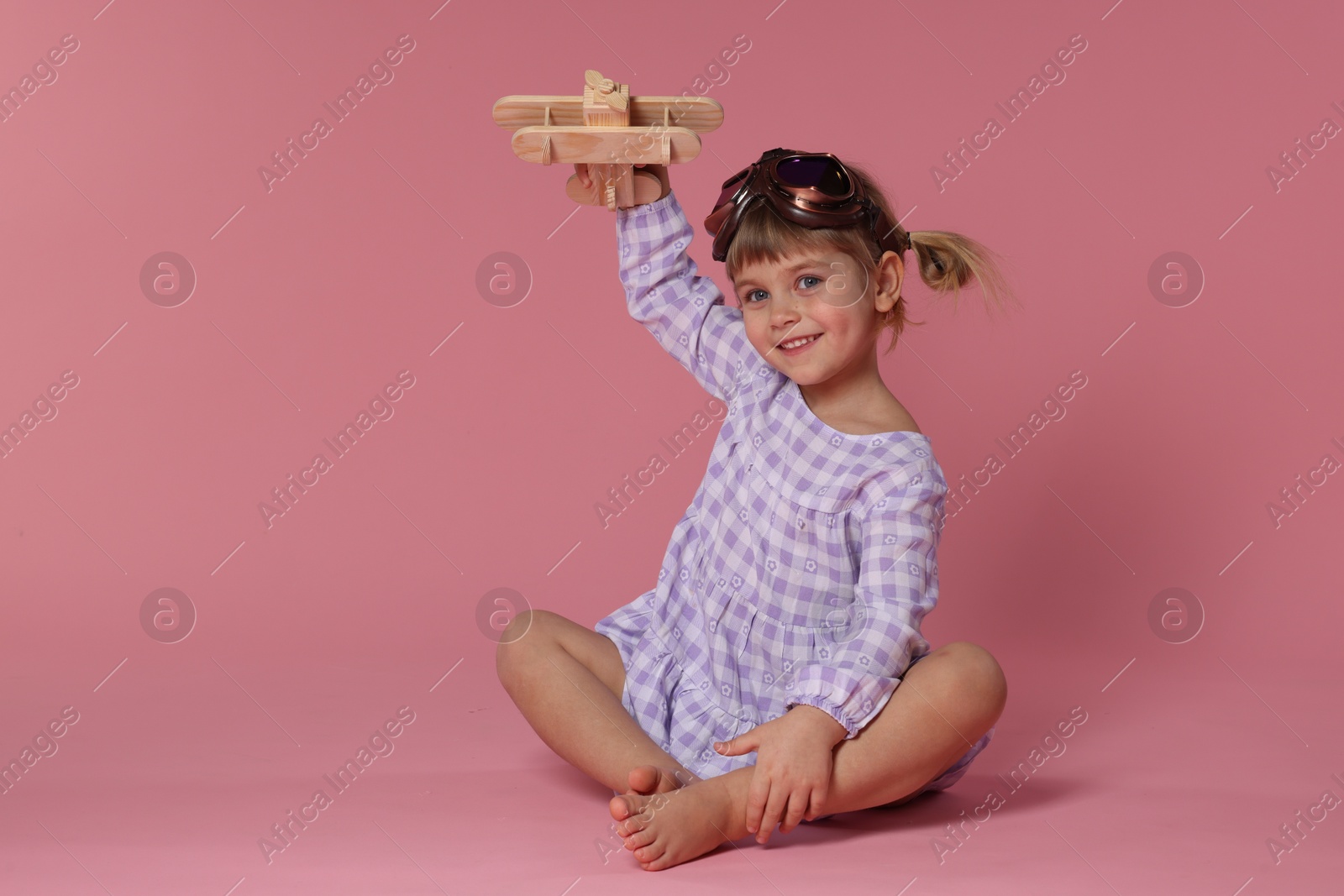 Photo of Happy little girl playing with toy plane on pink background. Space for text