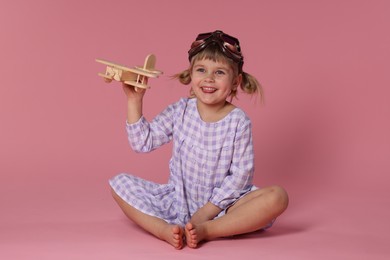 Photo of Happy little girl playing with toy plane on pink background