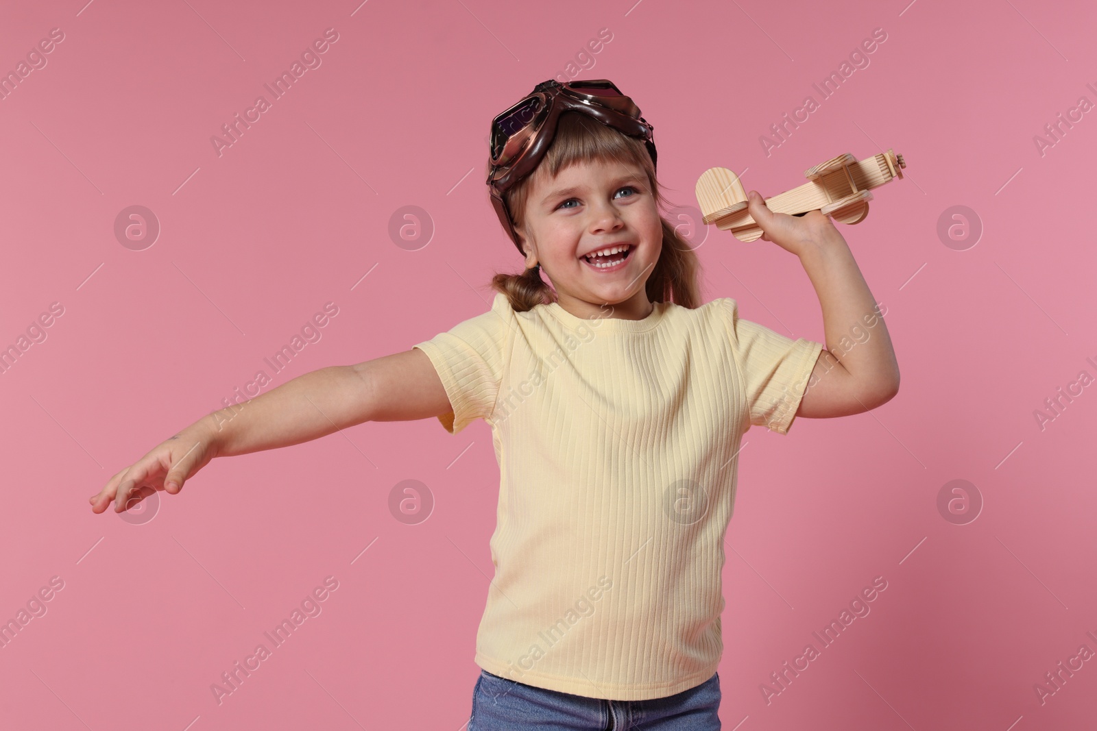 Photo of Happy little girl playing with toy plane on pink background