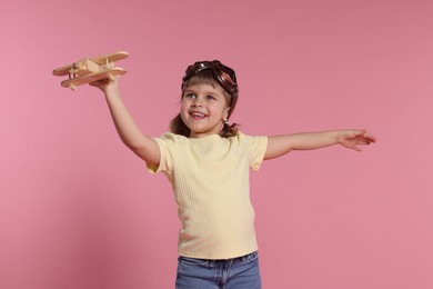 Photo of Happy little girl playing with toy plane on pink background