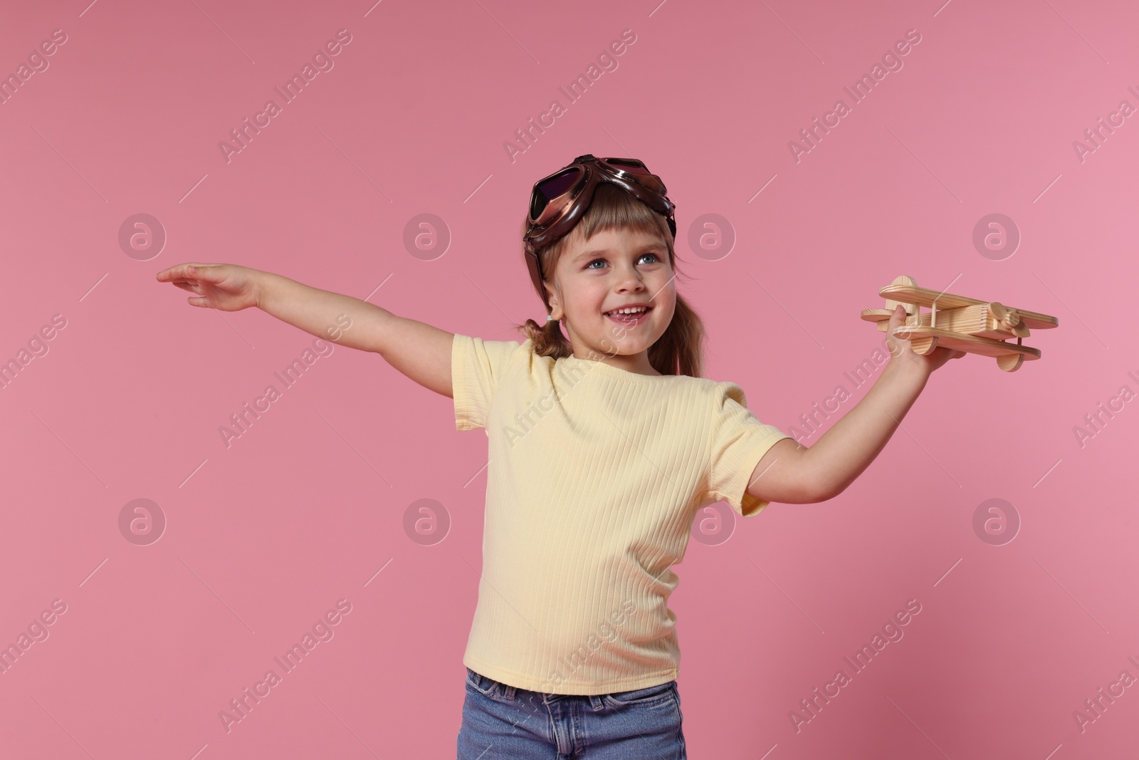 Photo of Happy little girl playing with toy plane on pink background