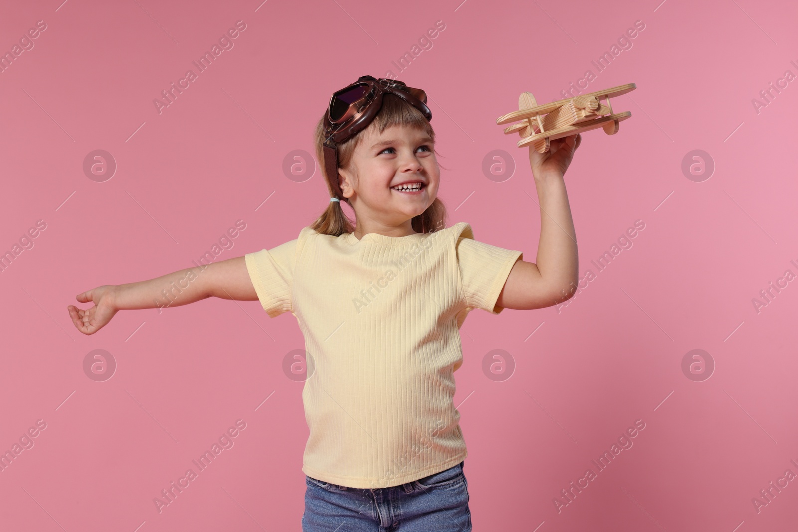 Photo of Happy little girl playing with toy plane on pink background