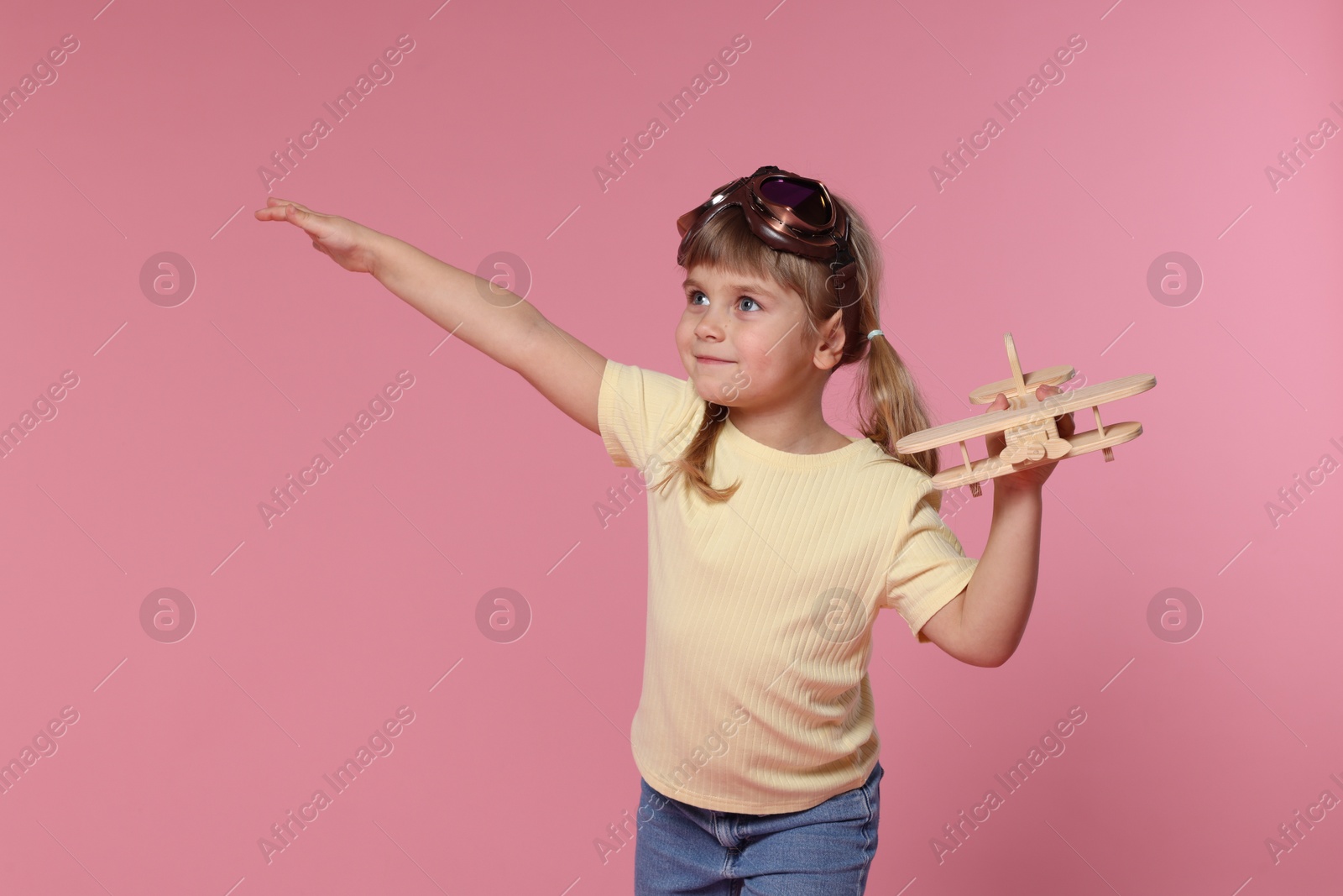 Photo of Cute little girl playing with toy plane on pink background