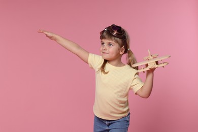 Cute little girl playing with toy plane on pink background