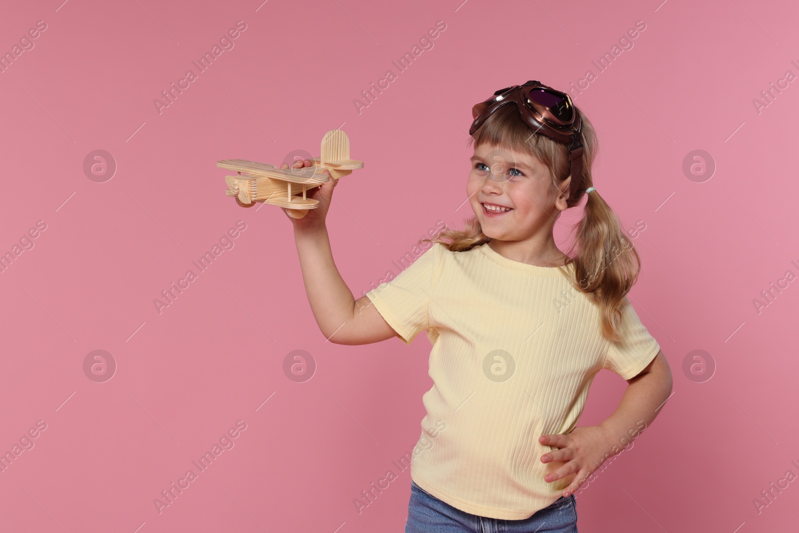 Photo of Happy little girl playing with toy plane on pink background. Space for text