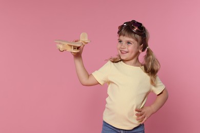 Happy little girl playing with toy plane on pink background. Space for text