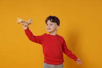 Cute little boy playing with toy plane on orange background