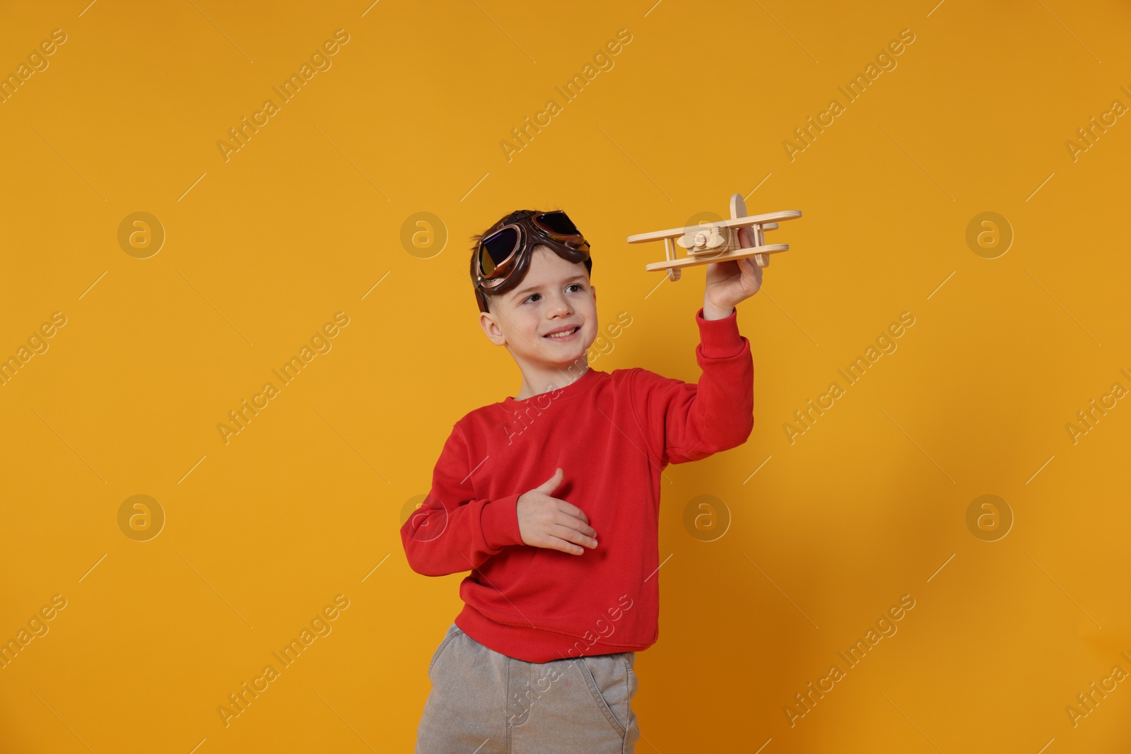 Photo of Happy little boy playing with toy plane on orange background