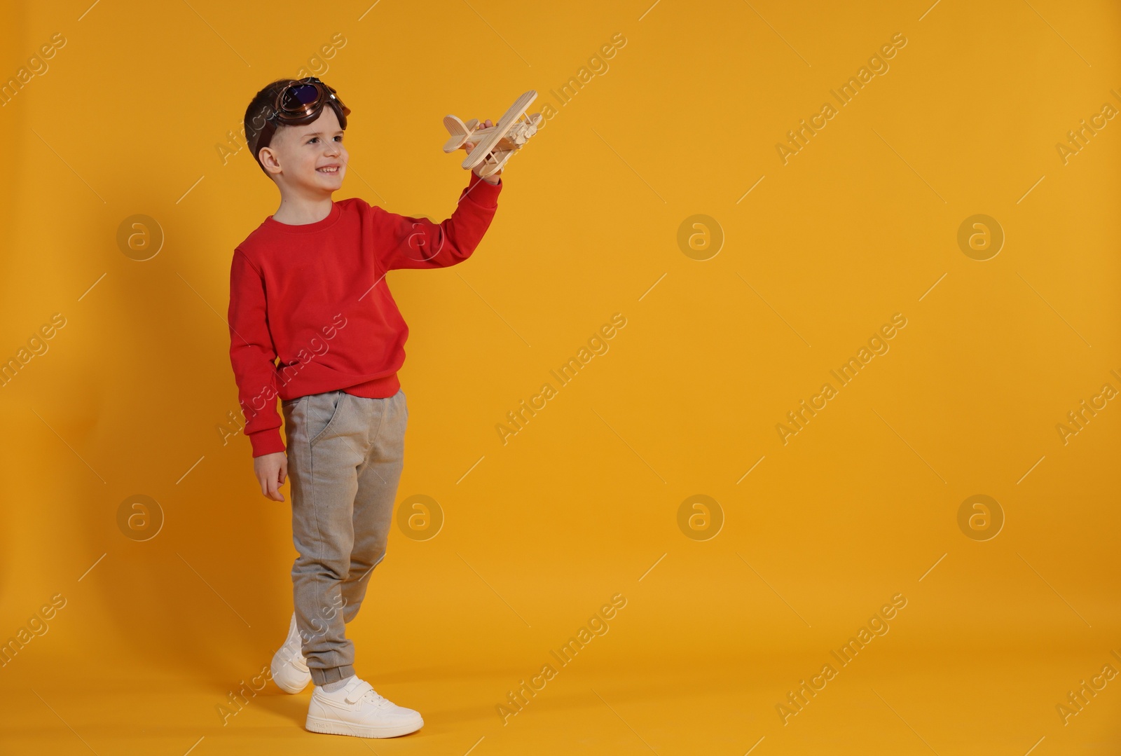 Photo of Happy little boy playing with toy plane on orange background. Space for text