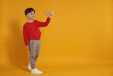 Happy little boy playing with toy plane on orange background. Space for text