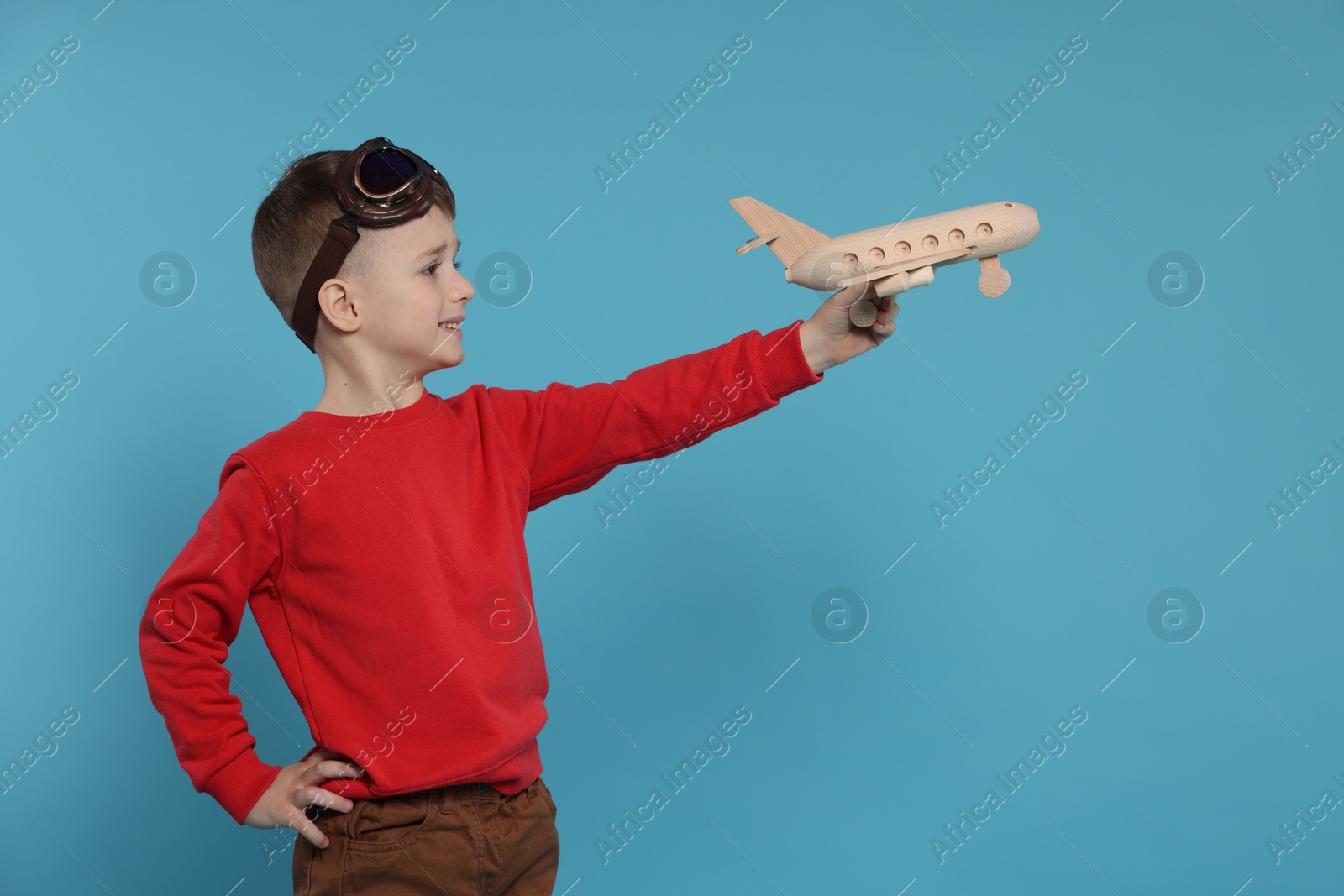 Photo of Happy little boy playing with toy plane on light blue background. Space for text