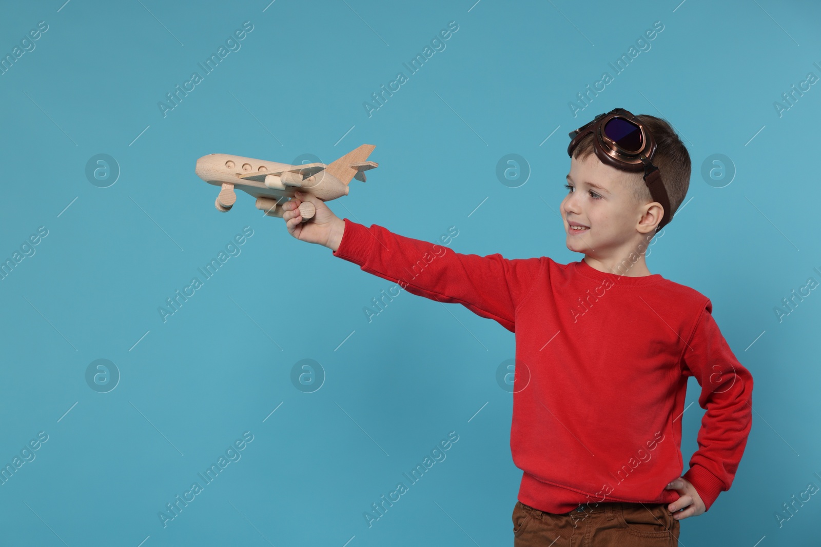 Photo of Happy little boy playing with toy plane on light blue background. Space for text