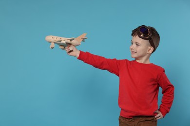 Photo of Happy little boy playing with toy plane on light blue background. Space for text