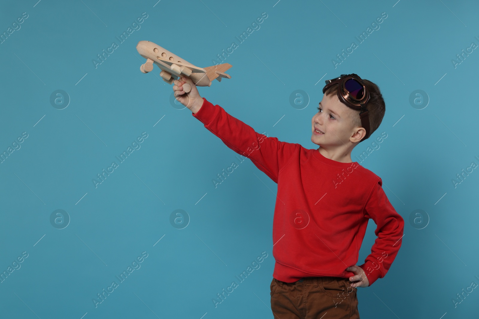 Photo of Happy little boy playing with toy plane on light blue background. Space for text