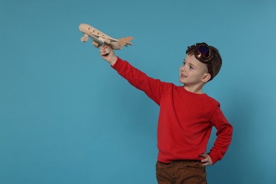 Happy little boy playing with toy plane on light blue background. Space for text