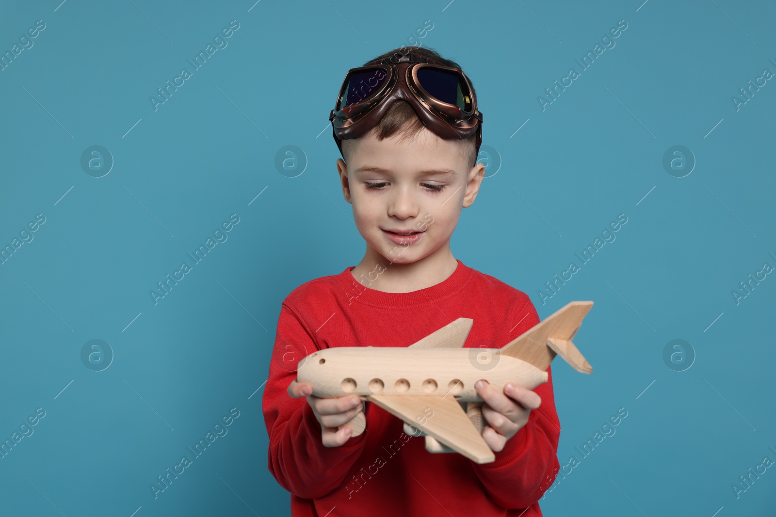 Photo of Cute little boy with toy plane on light blue background