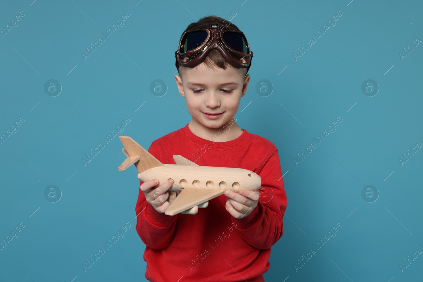 Photo of Cute little boy with toy plane on light blue background