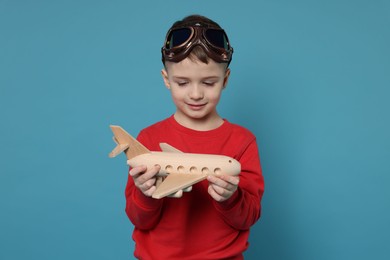 Cute little boy with toy plane on light blue background