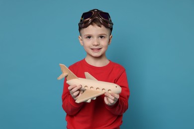 Happy little boy with toy plane on light blue background