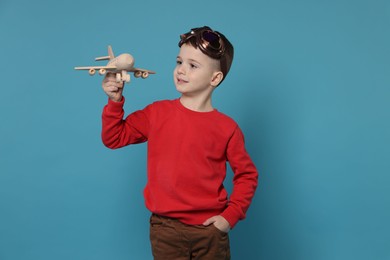 Photo of Happy little boy with toy plane on light blue background