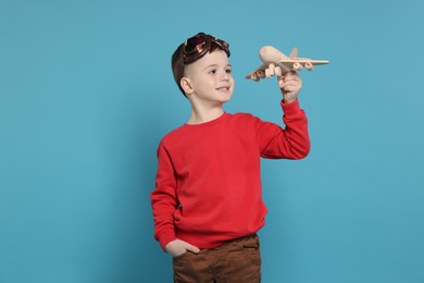 Photo of Happy little boy with toy plane on light blue background