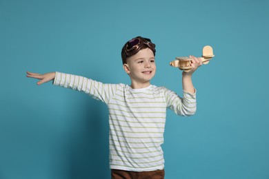 Happy little boy playing with toy plane on light blue background