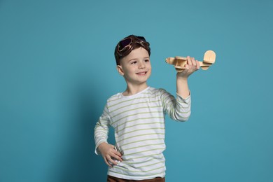 Photo of Happy little boy playing with toy plane on light blue background