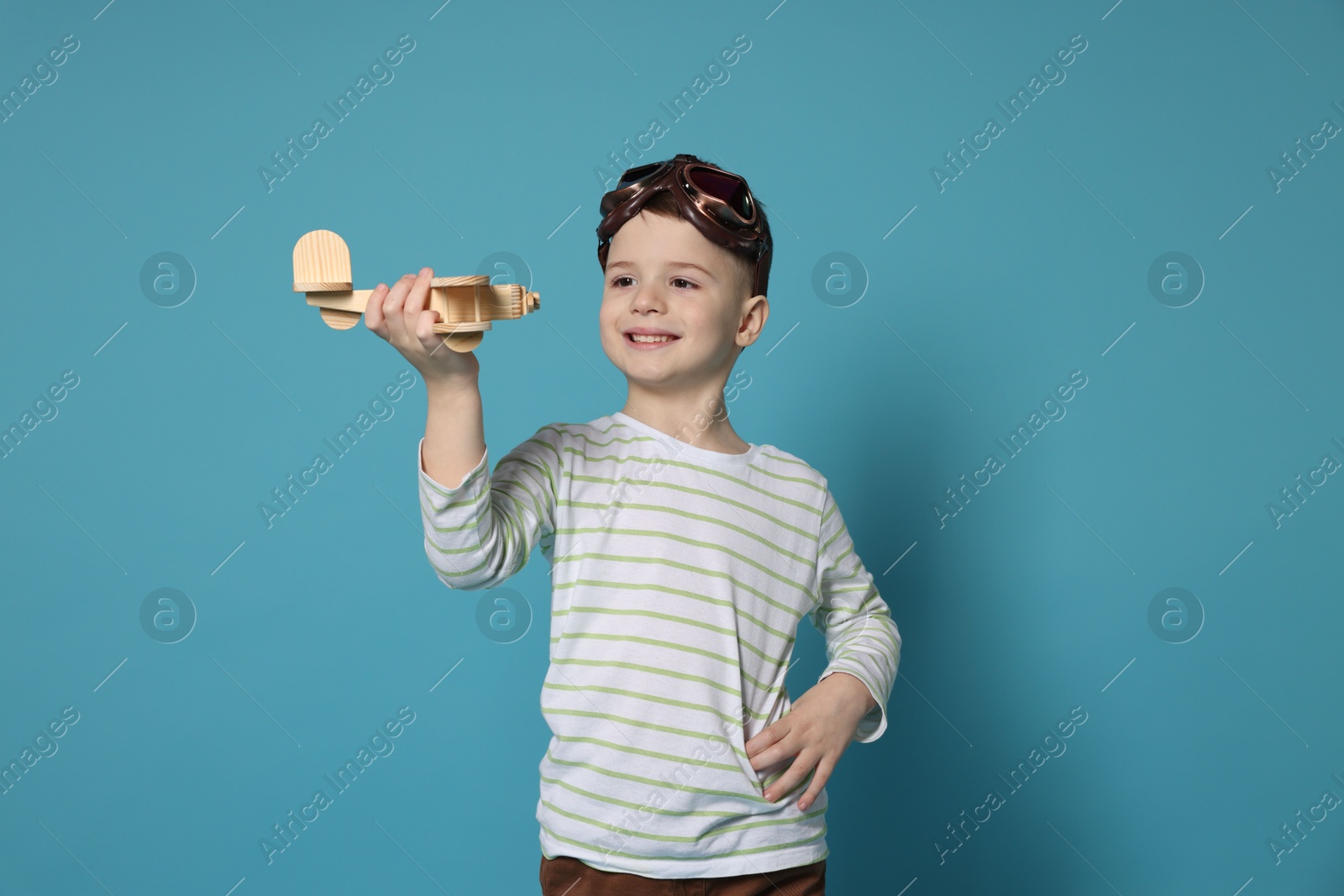 Photo of Happy little boy playing with toy plane on light blue background