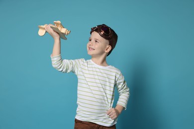 Happy little boy playing with toy plane on light blue background