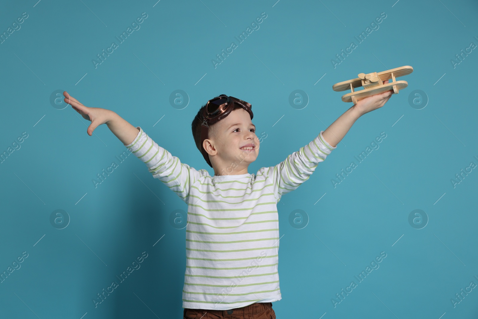 Photo of Happy little boy playing with toy plane on light blue background