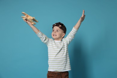 Happy little boy playing with toy plane on light blue background