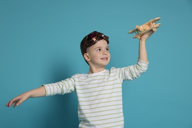 Happy little boy playing with toy plane on light blue background