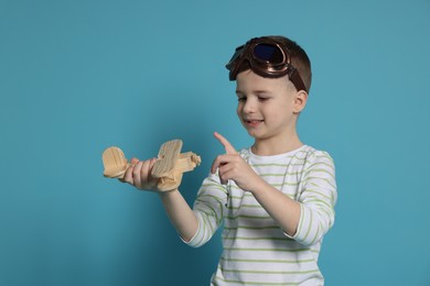 Photo of Happy little boy playing with toy plane on light blue background