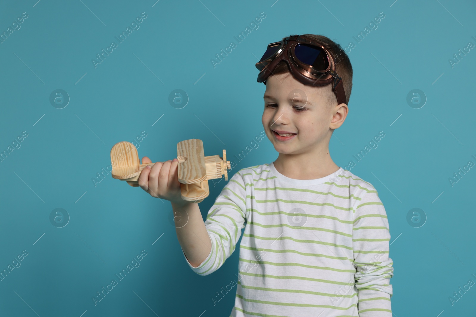 Photo of Happy little boy playing with toy plane on light blue background