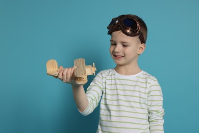 Photo of Happy little boy playing with toy plane on light blue background