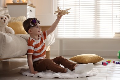 Happy little boy playing with toy plane at home