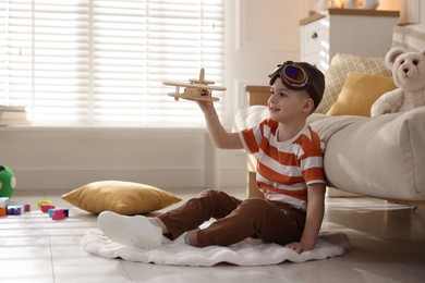 Happy little boy playing with toy plane at home