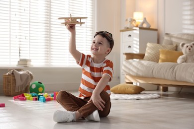 Photo of Happy little boy playing with toy plane at home