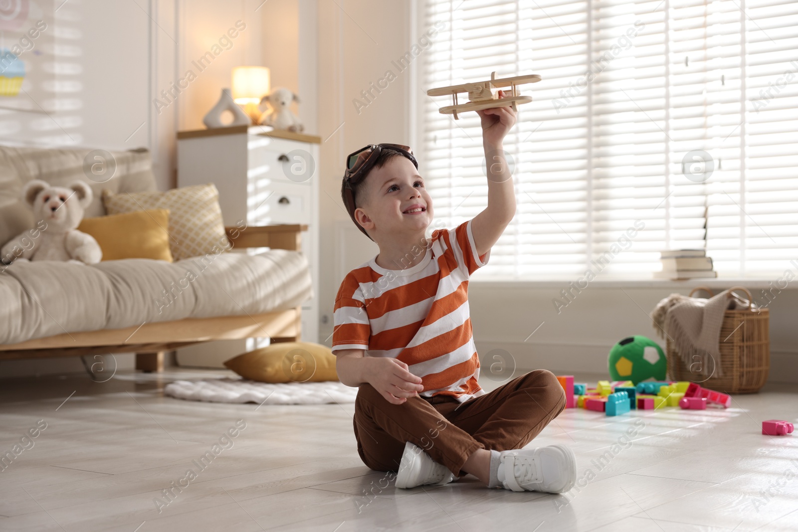 Photo of Happy little boy playing with toy plane at home