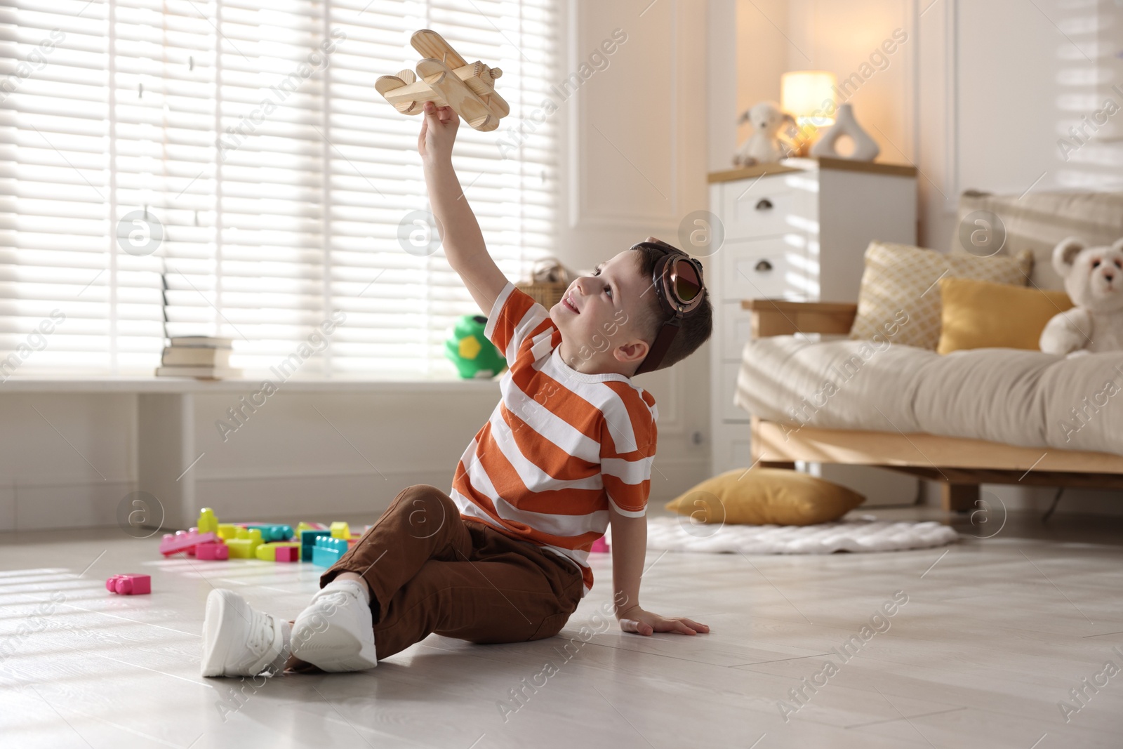 Photo of Happy little boy playing with toy plane at home