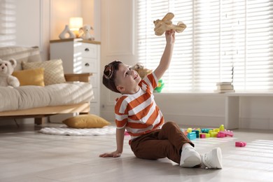 Photo of Happy little boy playing with toy plane at home