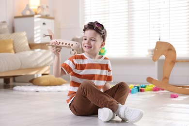 Happy little boy playing with toy plane at home